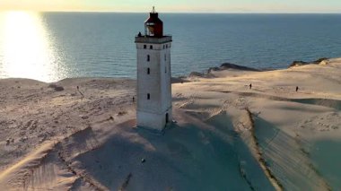Danimarka 'nın Jutland kentindeki Rubjerg Knude Fyr Deniz Feneri' nin büyüleyici manzarasını keşfedin. Sıcak günbatımı ikonik deniz fenerini yıkar..