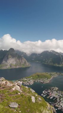 Yeşil tepelerin sakin sularla buluştuğu Lofoten Norveç 'teki el değmemiş bir fiyortu çevreleyen görkemli kayalıklar. Güneşli bir günde güzelliğe dalmış bir çift çarpıcı manzaranın tadını çıkarıyor..