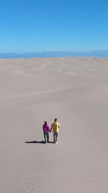 İki kişi, Danimarka, Rabjerg Mile Jutland 'ın engin kumullarında el ele yürürken sıcak güneş ışığının ve çarpıcı sahil manzarasının tadını çıkarıyorlar..