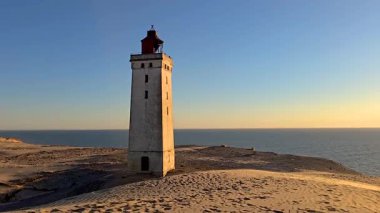 Danimarka 'nın Rubjerg Knude Jutland kıyı şeridinde çarpıcı bir günbatımına tanıklık edin. Ufukta gururla duran tarihi bir deniz feneri var.. 