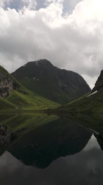 Sakin sularda yansıyan Norveç dağlarının nefes kesici güzelliğini deneyimleyin. yemyeşil vadiler ve dramatik tepeler huzurlu ve büyüleyici bir manzara yaratır, doğa severler için mükemmel..