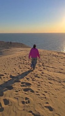 Huzurlu bir an, Danimarka Rubjerg Knude Jutland 'ın kumlu kumullarında gezinen bir yolcuyu yakalar. Altın gün batımı sakin denizi yansıtır.
