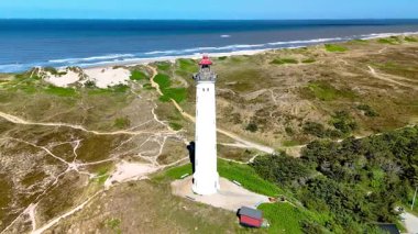 Danimarka 'nın Jutland kentindeki arka planda duran tarihi bir deniz fenerinin nefes kesici manzarası. Sakin deniz altın kumla buluşur ve mükemmel bir kaçış sunar. Lyngvig Deniz Feneri Hvide Sande