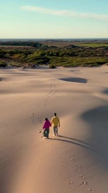 Danimarka 'nın Jutland kentindeki kumlu kumullarda el ele gezintiler. Güneş batıyor, manzaranın üzerine sıcak bir altın rengi serpiştiriyor, romantik bir atmosfer yaratıyor. Rabjerg Mil kum tepeciği