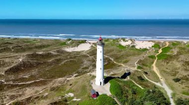 Danimarka, Jutland 'in doğal güzelliklerini tecrübe edin. Lyngvig Deniz feneri Hvide Sande, altın kumun denizle buluştuğu, simgesel deniz feneri tarafından çerçevelenmiş, açık mavi gökyüzüne karşı dik duran.