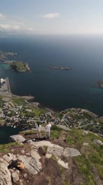 İki birey kayalık bir dağın tepesinde duruyor, sakin Norveç fiyortlarına ve dağınık adalara bakıyor. Reinebringen yürüyüşü Lofoten Norveç