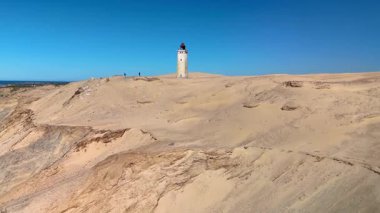 Danimarka 'nın Jutland kentindeki Rubjerg Knude Fyr Deniz Feneri' nin nefes kesici manzarasını deneyin. Altın kumlar durmaksızın uzanıyor, durgun mavi gökyüzü ve simgesel deniz feneri tarafından çerçeveleniyor..