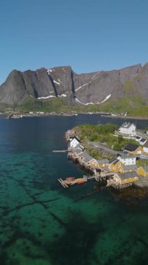 Lofoten Norveç 'in nefes kesici manzarasını deneyin, sakin sahil şeridi boyunca canlı sarı balıkçı kulübeleri sergileniyor..