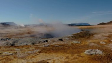 Hver İzlanda 'nın nefes kesici jeotermal özelliklerini keşfedin, açık mavi gökyüzü altında dinamik bir arazide buharlaşan bacalar ve renkli mineral yatakları gösterin..
