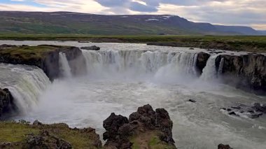 İzlanda 'nın engebeli arazisinde nefes kesici bir şelalenin güçlü akışını hissedin. Gök gürültülü su, yemyeşil yemyeşil Godafoss Şelalesi ile çevrili kayalık kayalıklardan aşağı dalıyor. 