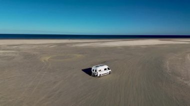 Danimarka 'daki Romo Lakolk plajının enginliğini deneyimleyin, açık mavi gökyüzünün altındaki altın kumlarda bir karavan sürüyordu. Sakin atmosfer rahatlamayı ve keşifleri davet ediyor..