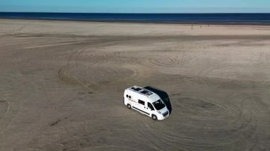 Danimarka 'nın Romo Lakolk plajında huzurlu bir günde kumlu sahilde giden bir karavan görülüyor. Geniş sahil manzaraları şaşırtıcı okyanus manzaraları sergiliyor, rahatlama ve macera için ideal..
