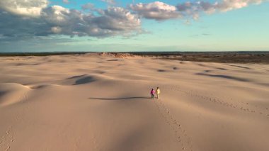 İki maceraperest, batan güneşin sıcacık ışığıyla aydınlanan Danimarka, Jutland 'ın dalgalı Rabjerg Mil kum tepelerinde geziniyor.