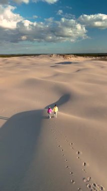 İki insan, muhteşem bir günbatımında Danimarka, Jutland, Rabjerg Mile 'ın engin kumullarında el ele dolaşır. Gökyüzünün yumuşak renkleri güzel bir şekilde altın kumlarla harmanlanır..