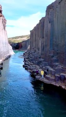 İzlanda, Studlagil Kanyonu 'ndaki turkuaz nehrin üzerinde yükselen eşsiz bazalt oluşumlarına hayret. Arkadaşlar nefes kesici manzaranın tadını çıkarırlar, bu doğal harikanın özünü yakalarlar..