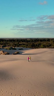 Danimarka 'nın Jutland kentindeki çarpıcı kum tepelerinde berrak mavi bir gökyüzünün altında iki kişi rahatça geziniyor. Altın kumlar ve yemyeşil yeşil sakin doğal bir zemin oluşturur. Rabjerg Mil kum tepeleri