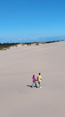 Danimarka 'nın Rabjerg Mile Jutland kentindeki kumullarda el ele yürüyen iki kişi. Parlak güneş ışığı, doğadaki sakin günleri için huzurlu bir atmosfer yaratıyor..