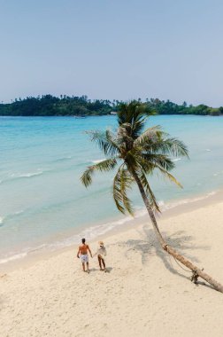 İki insan temiz mavi sular ve yemyeşil sularla çevrili kumlu bir sahilde huzurlu bir yürüyüşün tadını çıkarıyor. İlahi ayar, Koh Kood Tayland 'da mükemmel bir tropikal kaçamağın özünü yakalıyor.