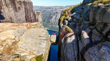 Tırmanışçıların Norveç 'in Kjeragbolten Lysefjord kentindeki sakin bir fiyordun üzerindeki sarp kayalıklar boyunca macerayı kucakladıkları heyecan verici bir an.