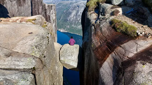 Maceracı bir birey, Norveç 'in görkemli fiyortlarının nefes kesici manzaralarıyla çevrili iki dik uçurum arasında asılı duran dev bir kayanın üzerinde oturur. Kjeragbolten Lysefjord, Norveç