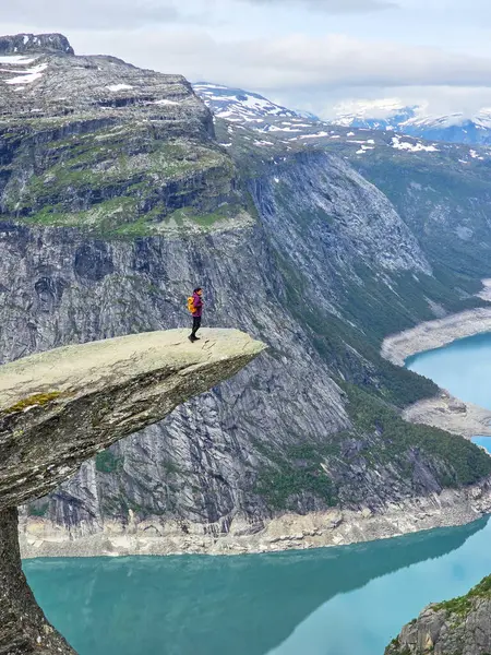 Yalnız bir yürüyüşçü dramatik bir uçurumun kenarında duruyor, Norveç 'in turkuaz fiyortlarından bakıyor. Norveç 'te Trolltunga yürüyüşü