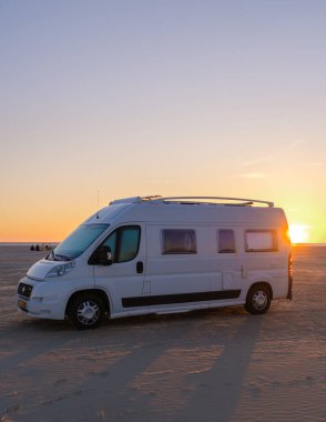 Canlı bir günbatımında Danimarka sahilinin kumlu sahillerine park etmiş bir karavan. Sıcak renkler gökyüzünü, Lakolk Strand ve Romo Danimarka 'yı doldururken dalgalar yavaşça kıyıya vurur.