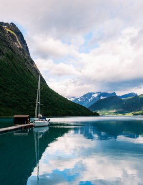 Norveç 'in Norangsfjorden kentindeki ahşap bir rıhtımda, heybetli dağlar ve sersemletici bir Norveç fiyordunda sakin sularla çevrili bir yat huzur içinde dinleniyor..