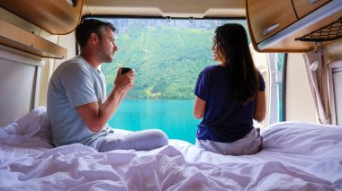 Bir çift, Norveç 'in Lovatnet kentindeki aydınlık bir sabah boyunca Norveç' te yemyeşil dağlarla çevrili muhteşem fiyortları izlerken karavanın içinde huzurlu bir anı paylaşıyor.