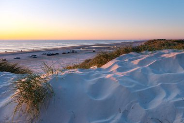 Danimarka 'daki bu sakin plaj sakin sularda yumuşak kum tepeleri ve renkli bir günbatımı sergiliyor. Ziyaretçiler huzurlu bir akşamın tadını çıkarıyorlar, Vejers Strand plajı.