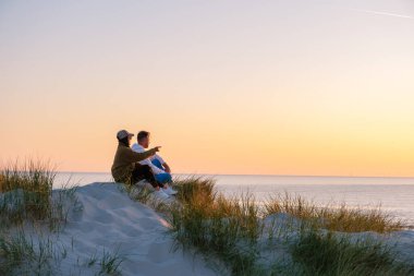 Danimarka 'daki yemyeşil kum tepelerinin ortasında, güneş dingin okyanusun üzerinde batarken bir çift birlikte ufku işaret ederek rahatlıyor. Gökyüzü sıcak renklerden oluşan bir tuvale dönüşür. Vejers Strand Sahili