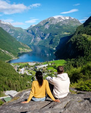 Bir çift Norveç 'teki göz kamaştırıcı Geirangerfjord' a bakan kayalık bir çıkıntıda dinleniyor. Yeşillik ve görkemli dağlar etraflarını sararak doğada mükemmel bir kaçış yaratıyor..