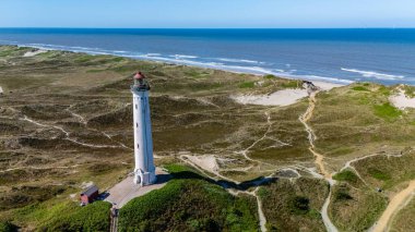 Danimarka 'nın manzaralı sahil şeridini gözler önüne seren nefes kesici bir manzara. Etrafı kum tepeleri ve sakin mavi sularla çevrili uzun bir deniz feneri..