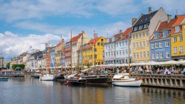 Nyhavn, Kopenhag, Danimarka, 12 Temmuz 204: Canlı evler Danimarka 'nın bir şehrindeki pitoresk kanalda yüzüyor ve yelkenliler yavaşça suda sallanıyor. Ziyaretçiler gezintileri ve açık hava yemeklerini severler. 