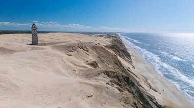 Görkemli bir şekilde ayakta duran bir deniz feneri Danimarka 'nın çarpıcı kıyı manzarasını gözler önüne seriyor. Ziyaretçiler, Kum tepelerini, Rubjerg Knude deniz fenerini, Kuzey Jutland Danimarka 'yı keşfediyor