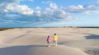 Mavi gökyüzünde uçuşan kabarık bulutlar gibi Danimarka 'daki kumullarda el ele romantik bir yürüyüş yapan bir çift. Doğada sakin bir an, Rabjerg Mile Dunes