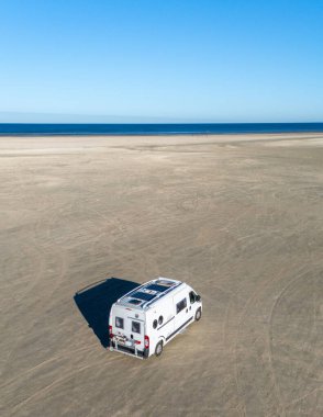 Romo Danimarka 'nın pürüzsüz kumlu sahiline park etmiş bir karavan. Parlak güneş ışığında güneşleniyor. Uçsuz bucaksız kıyı şeridi ufka doğru uzanıyor, sakin kıyı manzaraları sunuyor, kaçmak için ideal..