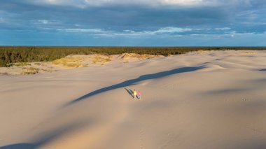 Danimarka 'nın engin altın kum tepecikleri üzerinde yürüyen iki kişi gece boyunca çarpıcı mavi gökyüzü altında uzun gölgeler bırakarak Danimarka' nın Rabjerg Mile Kumulları,.