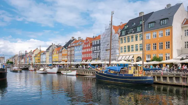 Nyhavn, Kopenhag, Danimarka, 12 Temmuz 204, parlak renkli binaların kanalı kapladığı yer. İnsanlar açık hava kafelerinde toplanıp manzaranın tadını çıkarırken kayıklar suda hafifçe sallanıyor..