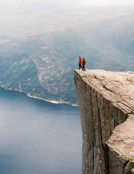 İki yürüyüşçü ikonik Preikestolen Minber Kayası 'nın tepesinde dikilip aşağıdaki muhteşem fiyorda bakıyorlar. Norveç 'te dramatik uçurumlar ve verimli yeşilliklerle çevrili
