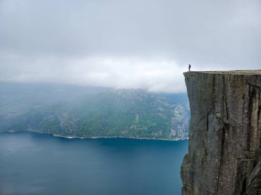 Lysefjord Norveç 'in çarpıcı mavi sularına tepeden bakan, Preikestolen' in kıyısında tek başına bir yürüyüşçü duruyor.