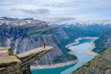 Norveç 'teki nefes kesici Trolltunga uçurumunun kenarında, sakin bir göle ve görkemli dağlara bakan iki maceracı duruyor. Bu el değmemiş alan saf güzelliği gösteriyor..