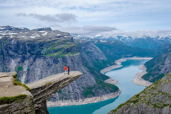 Norveç 'teki nefes kesici Trolltunga uçurumunun kenarında, sakin bir göle ve görkemli dağlara bakan iki maceracı duruyor. Bu el değmemiş alan saf güzelliği gösteriyor..