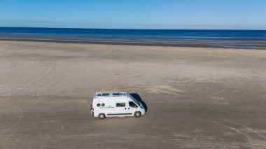 Bir karavan, Romo Danimarka 'da sakin kumlu bir plaj boyunca seyahat ediyor. Sahil şeridinin uçsuz bucaksız uzantısı güneş ışığıyla yıkanarak huzurlu bir atmosfer yaratıyor. C