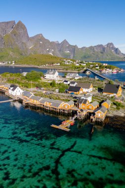 Lofoten, parlak mavi gökyüzünün altında görkemli dağlarla çevrili su boyunca geleneksel ahşap kazıcıları sergiliyor..