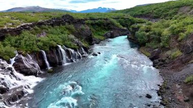 İzlanda 'daki Barnafoss ve Hraunfossar' ın büyüleyici turkuaz sularını keşfedin. Burada eşsiz kaya oluşumları yemyeşil ve görkemli dağlarla nefes kesici bir doğa harikası içinde buluşur..