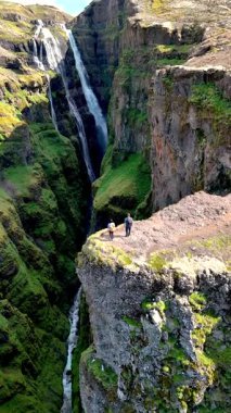 Macera avcıları dramatik uçurumların kenarında dikilirken çarpıcı bir şelale aşağıdaki yemyeşil vadiye dökülüyor. İzlanda 'daki Glymur şelalesi kanyonu
