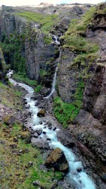 İzlanda 'nın uzak kanyonunun nefes kesici güzelliğini deneyimleyin. Parlak bir şelale engebeli kayalıkların üzerinden canlı bir dereye dökülüyor. İzlanda 'daki Glymur şelalesi kanyonu