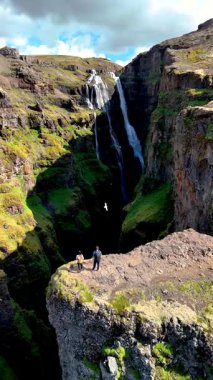 İzlanda 'nın nefes kesici güzelliğini keşfedin, derin bir kanyona dökülen çarpıcı bir şelale, İzlanda' daki kayalık bir kanyonun manzarasına hayran gezginler,