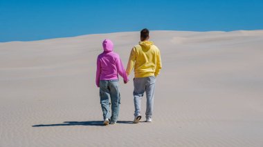Genç bir çift, Danimarka 'nın Rabjerg Mile kumullarındaki sakin kum tepelerinde el ele dolaşarak sıcak güneşin tadını çıkarıyor. Huzurlu manzaranın tadını çıkarırlarken ayak izleri yollarını işaretler..