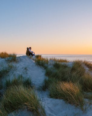 Çift, sallanan çimenler ve yumuşak kumlarla çevrili Danimarka sahillerinde huzurlu bir günbatımının tadını çıkarıyor. Alacakaranlığın ılık tonları doğayla bağlantı kurarken romantik bir atmosfer yaratıyor..